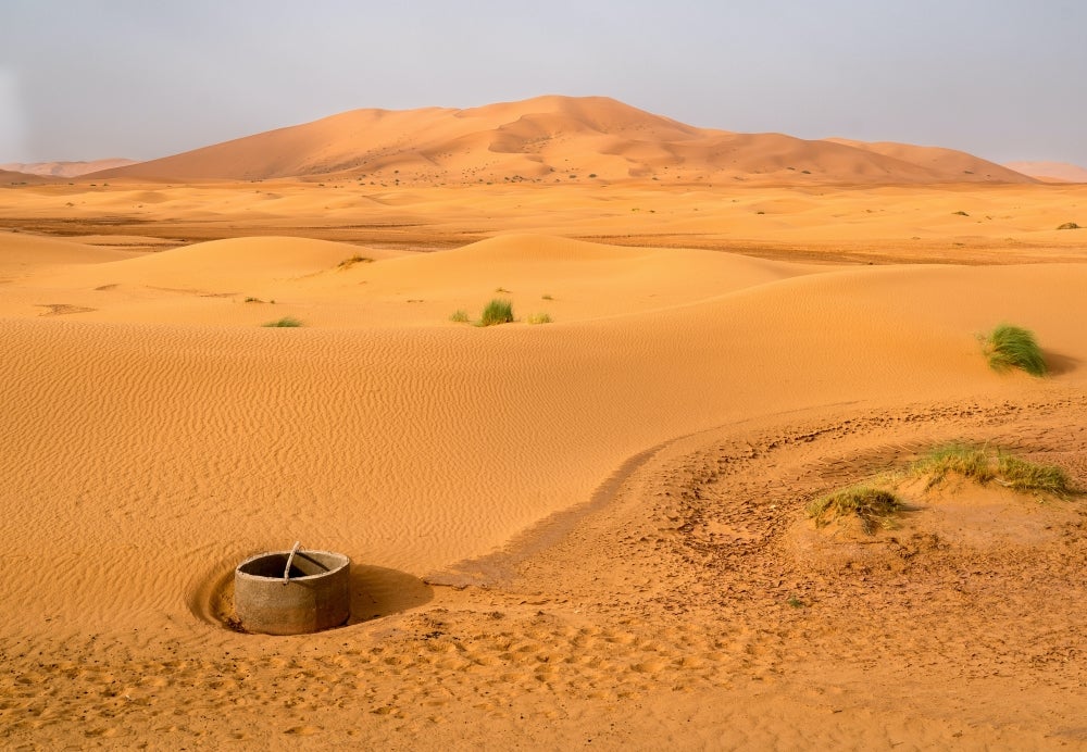 A concrete well and a few grassy tussocks with sand dunes in the background